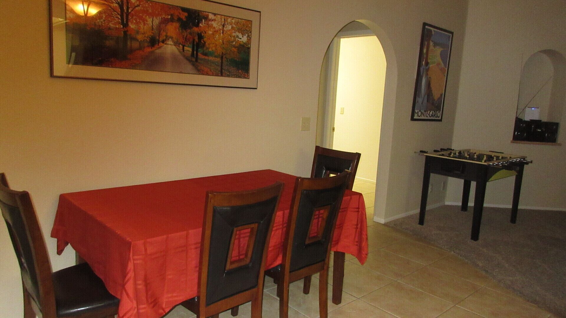 Un comedor con una mesa y sillas rojas, un cuadro sobre la mesa y una mesa de fútbol de mesa al fondo.