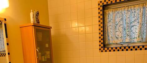 A bathroom with a toilet, a sink, a cabinet, and a window with patterned curtains.