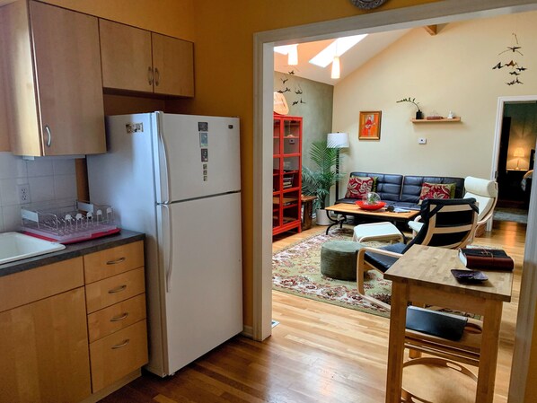 Une cuisine compacte avec des meubles en bois, un réfrigérateur blanc et un coin repas comprenant une bibliothèque rouge, une table et un canapé.