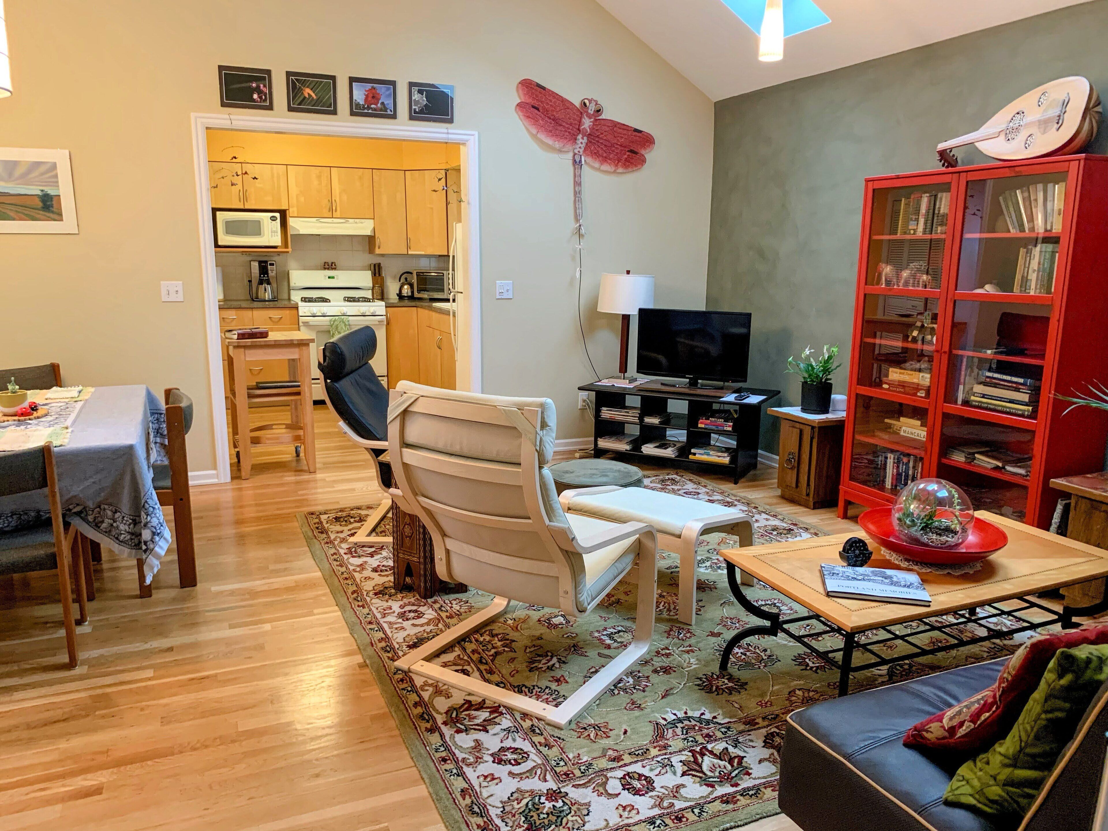 A living room with a sofa, a coffee table, a TV, a bookshelf, and a dining area with a table and chairs.