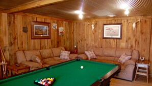 A pool table with a green felt surface, a sofa with patterned cushions, and a framed picture of Route 66 on the wall. - Peaceful Country Cottage with Game Room & Hot Tub (Beattyville)