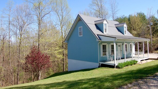 A single-story house with a porch, surrounded by trees and a grassy yard. - Peaceful Country Cottage with Game Room & Hot Tub (Beattyville)