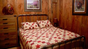 A wooden-paneled bedroom with a metal bed frame, a quilted bedspread, a wooden dresser, and framed pictures on the walls. - Peaceful Country Cottage with Game Room & Hot Tub (Beattyville)