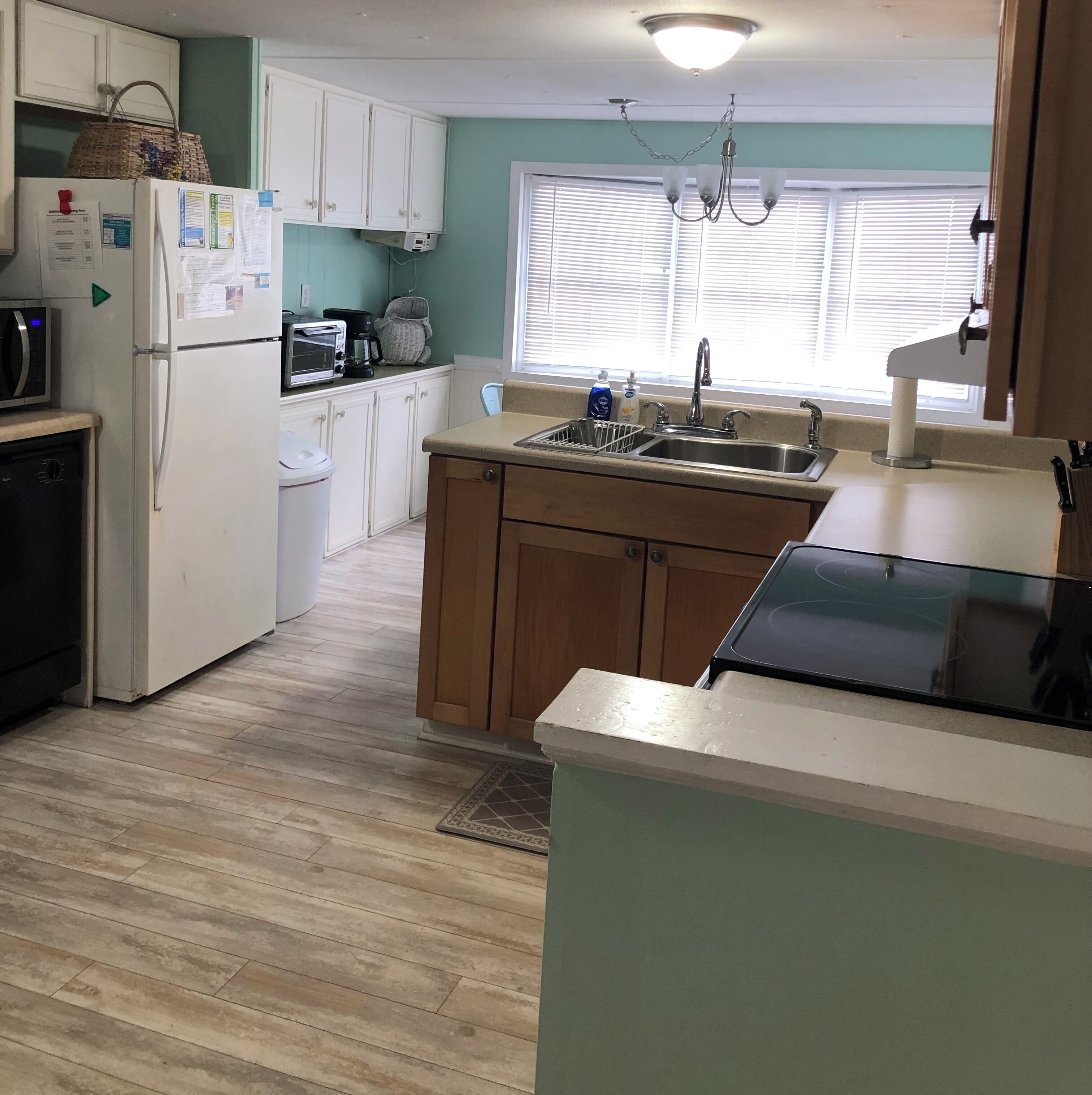 Una cocina compacta con gabinetes blancos, microondas integrado, refrigerador, cafetera y lavamanos.