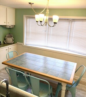 A dining area with a wooden table and teal chairs, a chandelier, and a window with blinds. - Ocean and Lake views, Pet friendly, Golf cart. (Myrtle Beach)
