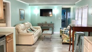 Uma sala de estar com sofá, mesa de centro e televisão na parede.