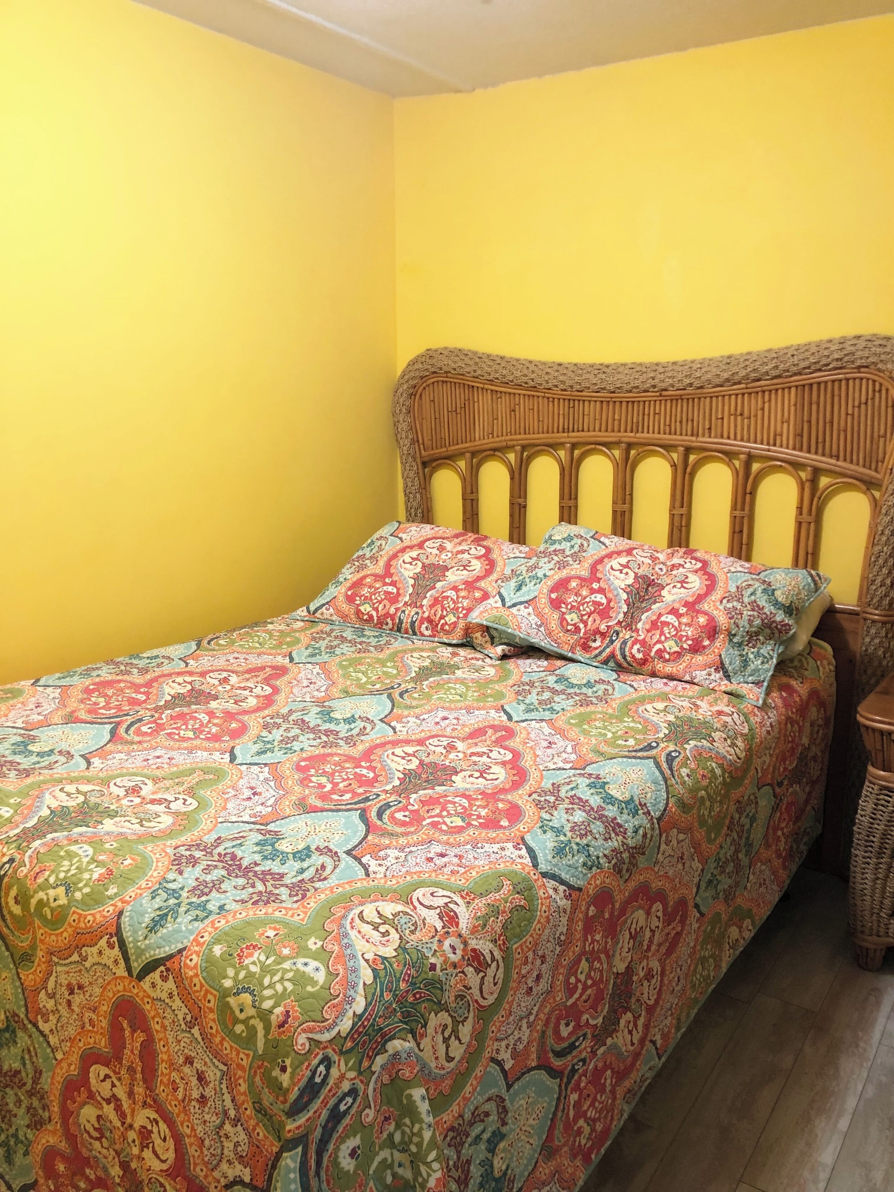 Een bed met een geboeide spreidekker in een kamer met gele wanden.