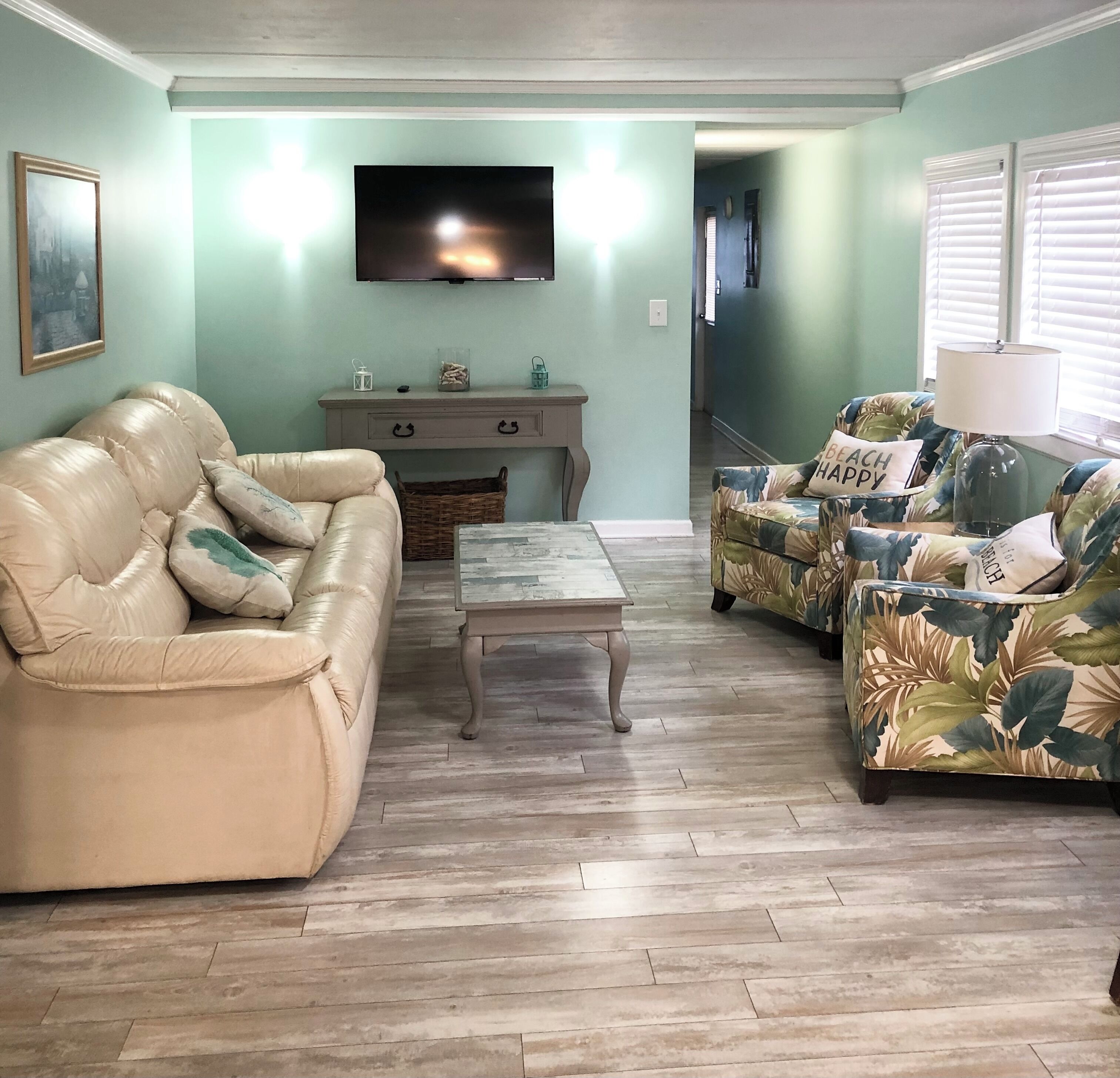 A living room with a beige sofa, a floral-patterned sofa, a wooden coffee table, and a television on the wall.
