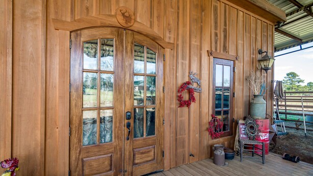 A wooden cabin with a large front door, a smaller door, and a porch area with a lantern and a sign.