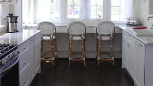 Une cuisine avec des meubles blancs, un fourneau et deux chaises en osier.