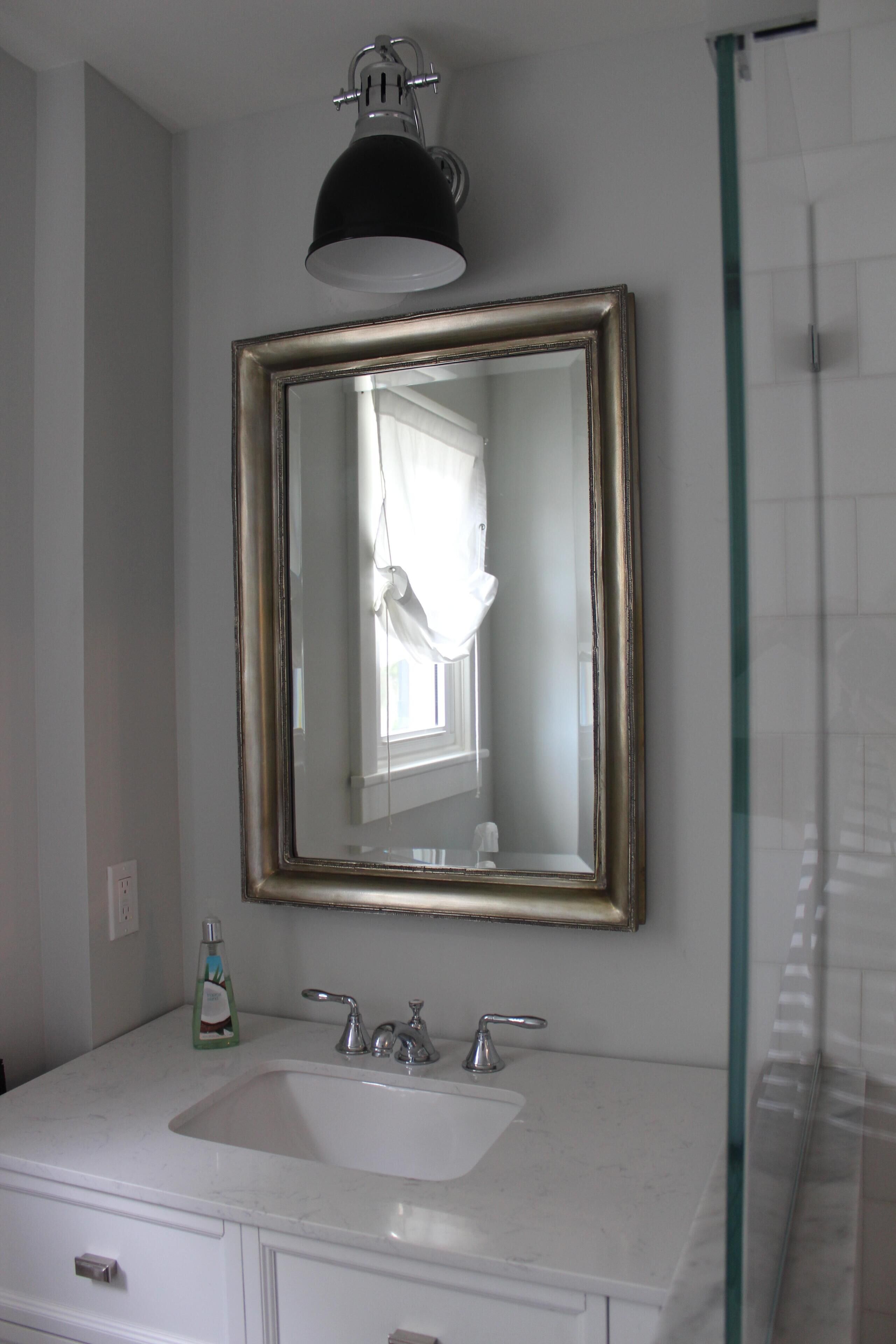 A bathroom with a white sink, two faucets, a mirror with a gold frame, and a black overhead light.
