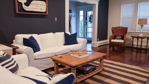 Un salon avec un canapé blanc, une table basse en bois et un tapis à rayures. On y trouve une chaise sur laquelle est apposée une plaque indiquant l’adresse « 820, avenue Sewall ».