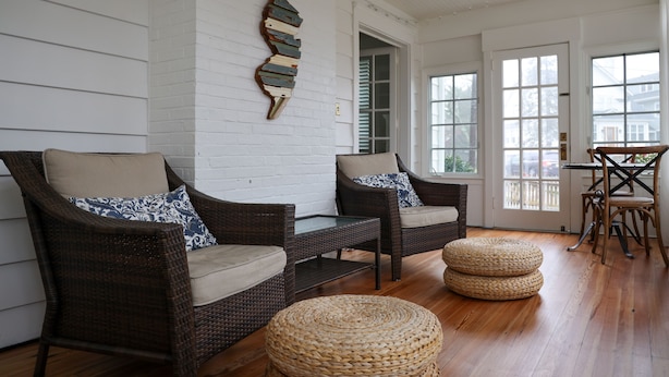 Une pièce comprenant deux fauteuils en osier avec des coussins, un pouf en fibres tressées et une table avec des chaises.