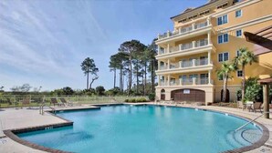 A hotel with a swimming pool, multiple balconies, and a clear sky.