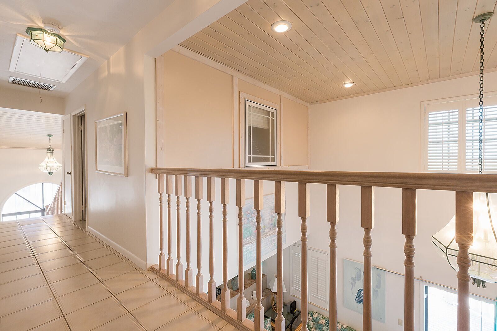 A spacious hallway with a wooden floor, a wooden railing, and a staircase leading to an upper level.
