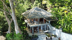 Ein reetgedecktes Bungalow mit Balkon, umgeben von üppiger Vegetation.