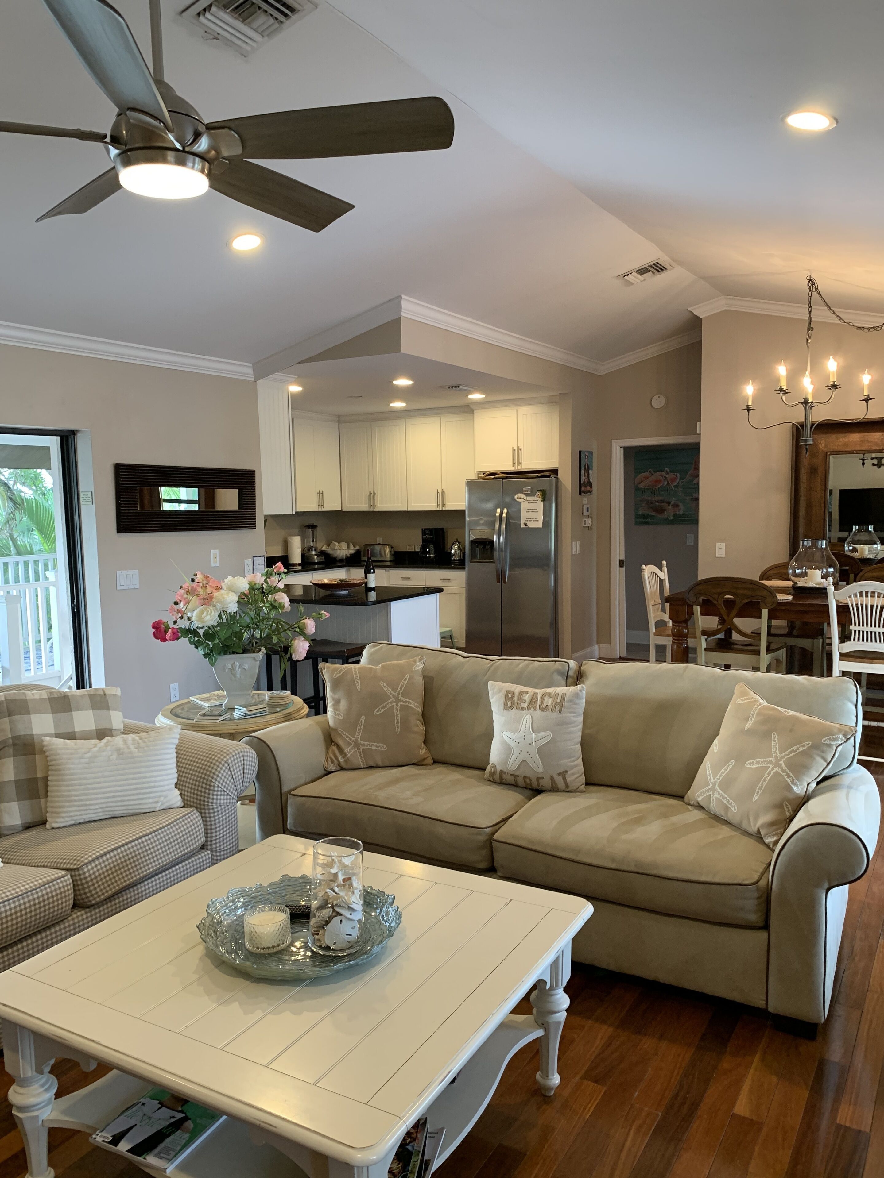 A modern living room with a beige sectional sofa, a white coffee table, and a dining area with a wooden table and chairs.