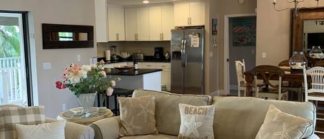 A modern living room with a beige sectional sofa, a white coffee table, and a dining area with a wooden table and chairs.