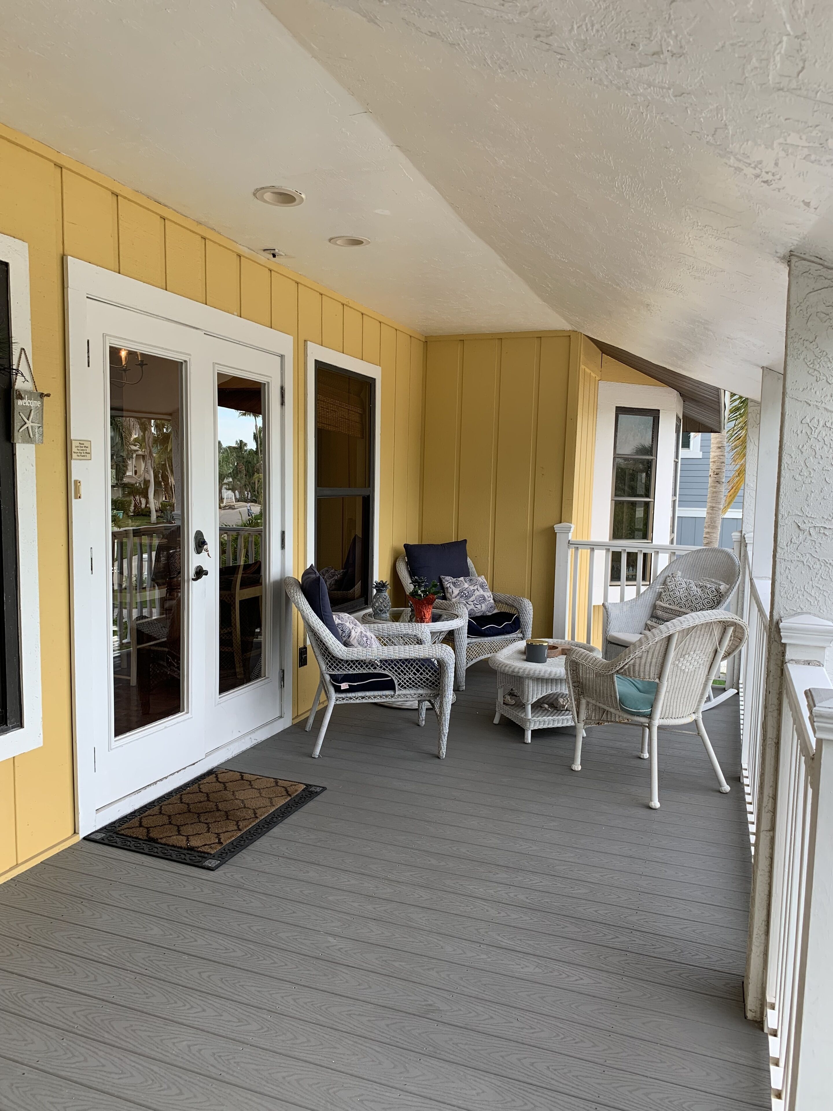 A covered porch with wicker furniture, a white door, and a small table.