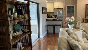A spacious living room with a wooden bookshelf, a checkered sofa, and a kitchen in the background.