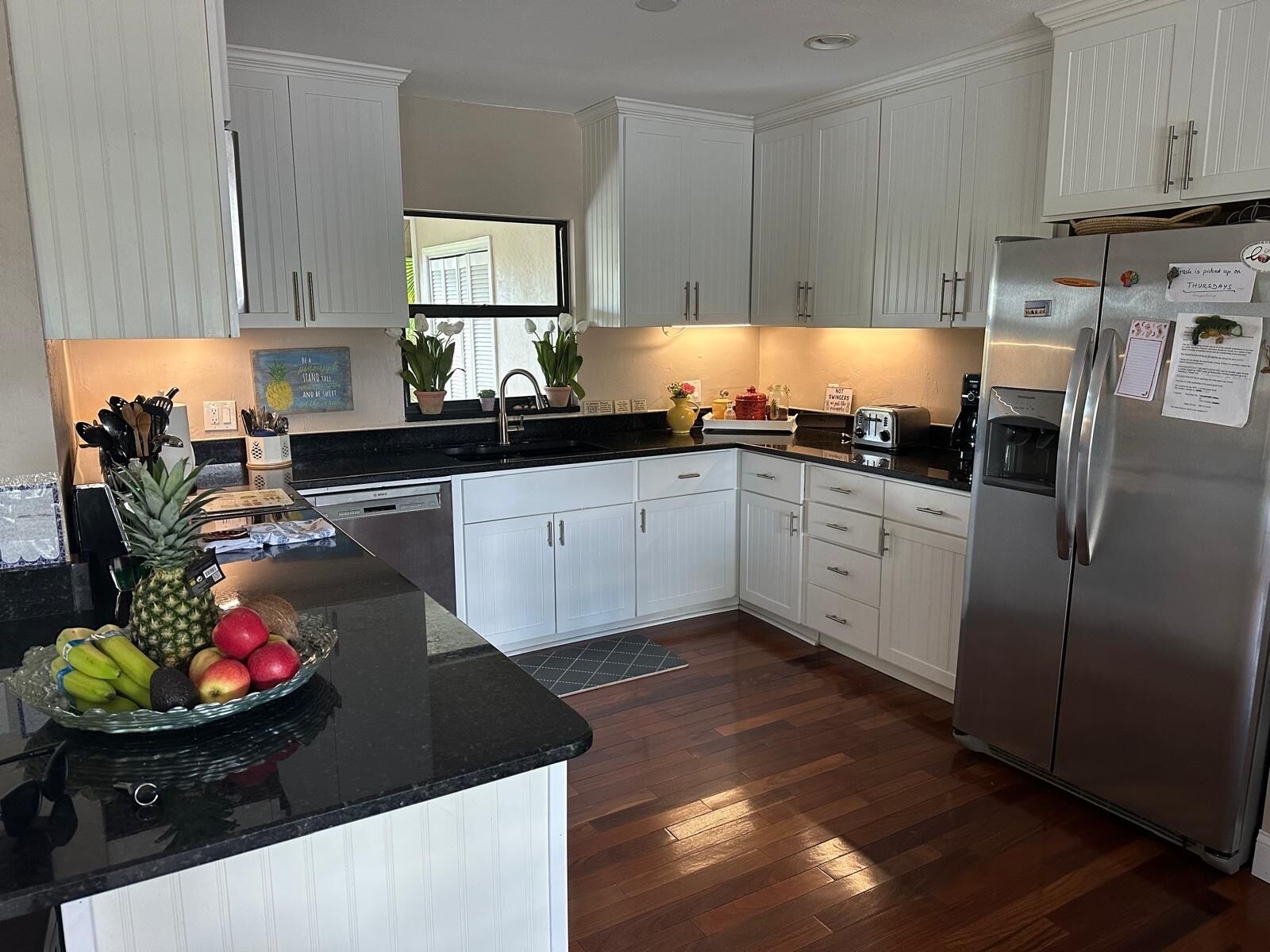 Una cocina moderna con armarios blancos, un refrigerador de acero inoxidable y un frutero sobre la encimera.