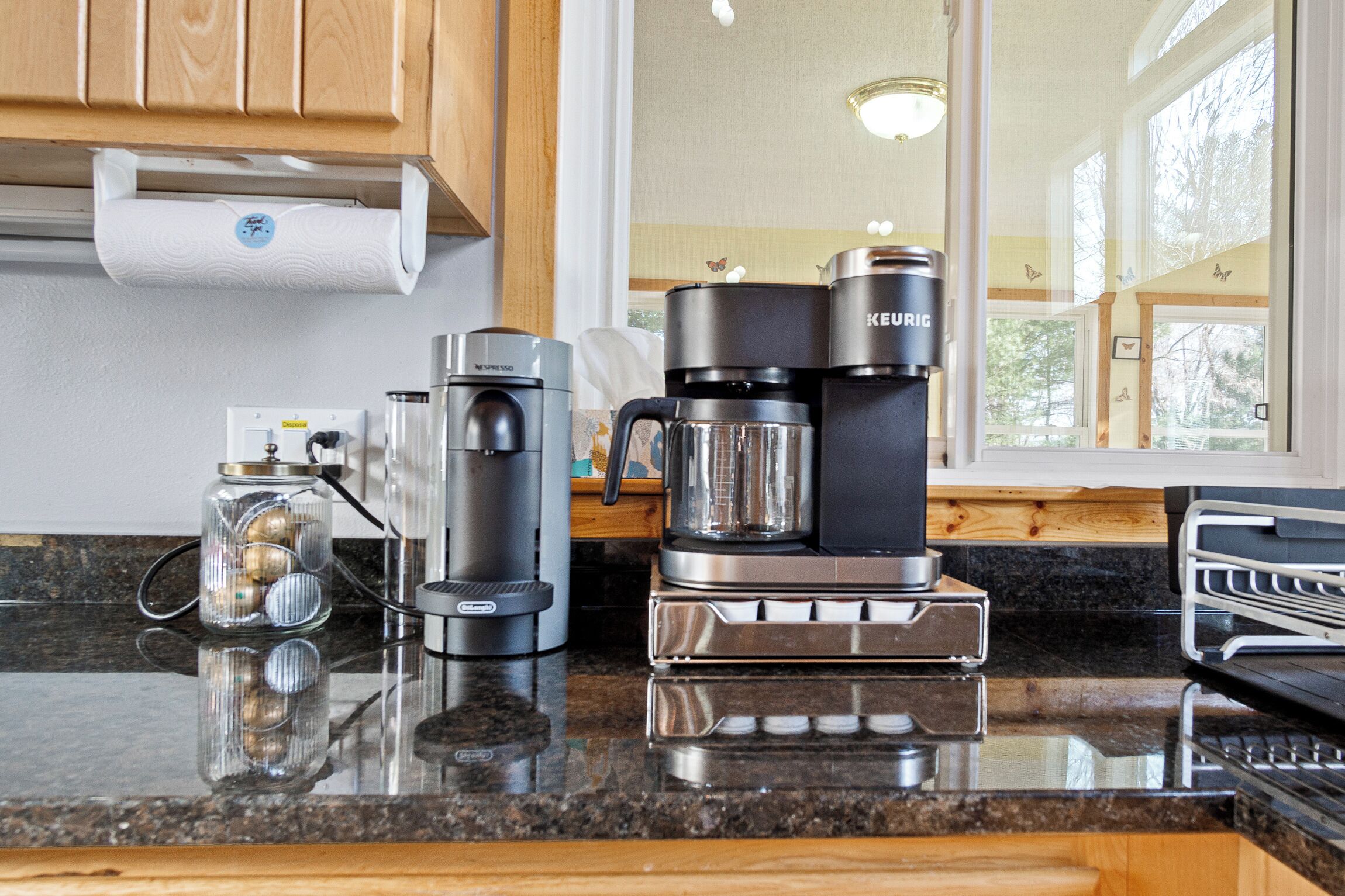 A kitchen with a coffee maker, a Keurig, and a glass jar with decorative items.