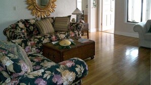 A living room with a floral sofa, a wooden coffee table, and a sunburst mirror.