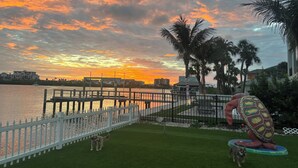 A waterfront view with a sunset, a white picket fence, and a turtle sculpture.