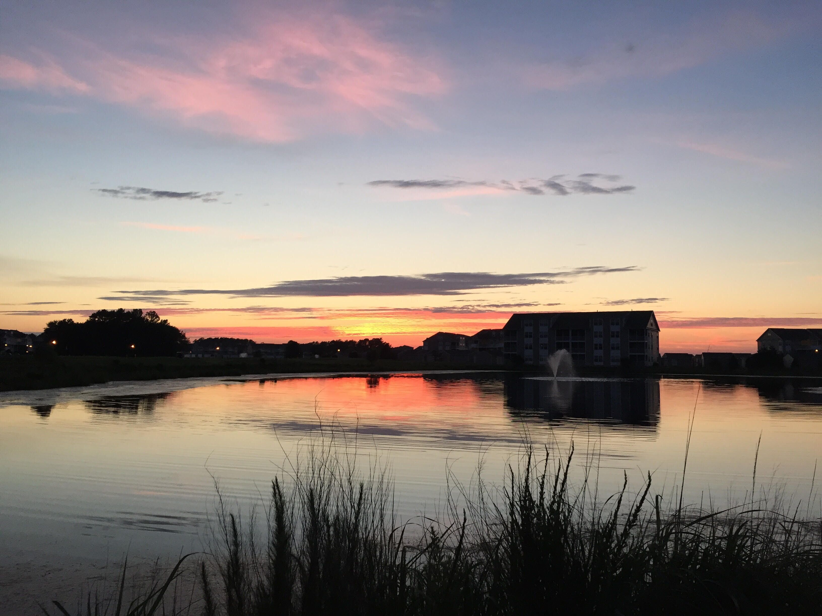 Tyyni järvi auringonlaskun aikaan, taustalla näkyy rakennuksia.