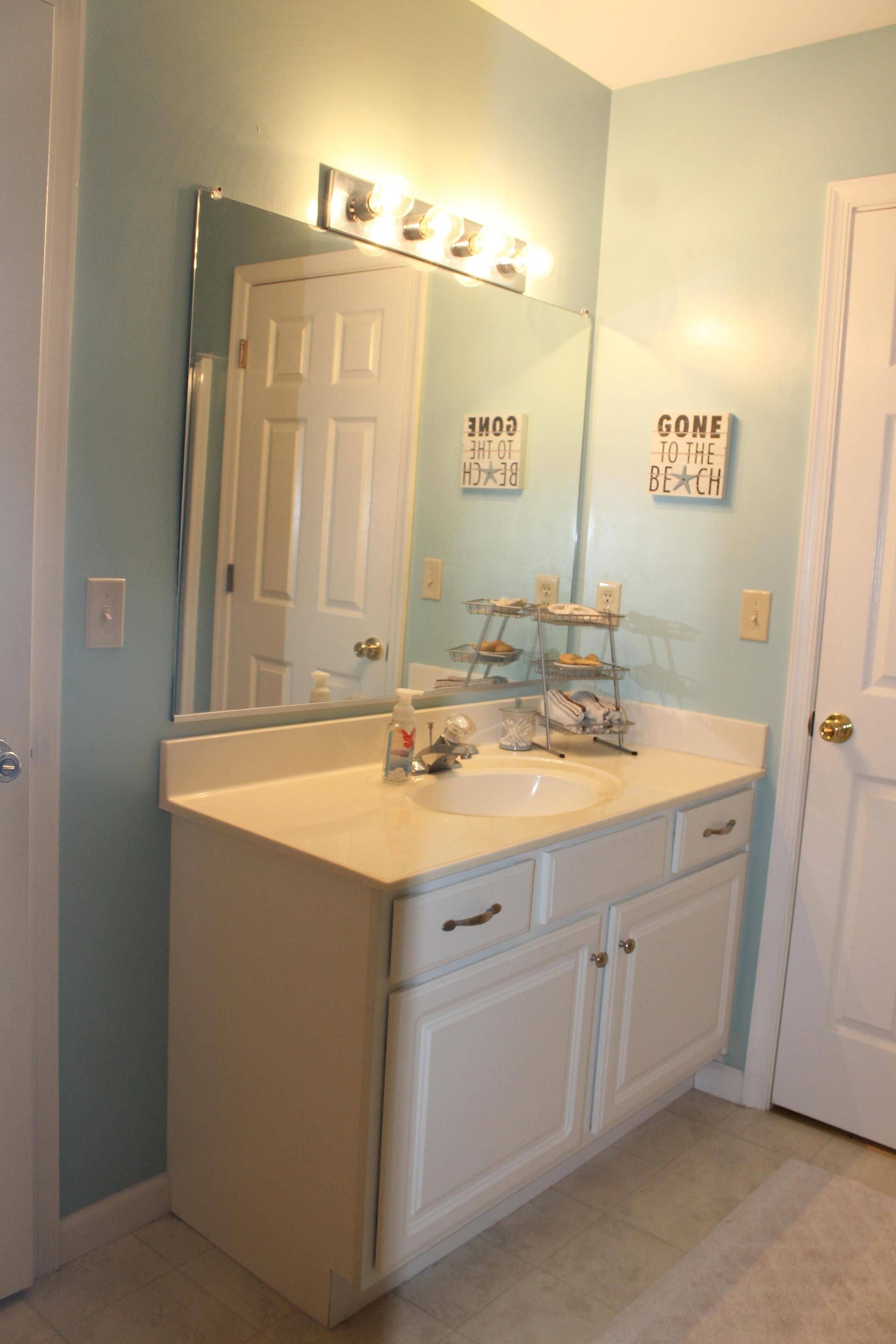 A bathroom with a white vanity, a large mirror, and a door with a light switch.