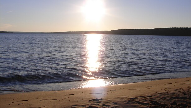 Una playa con cielo despejado y agua tranquila que refleja el sol.