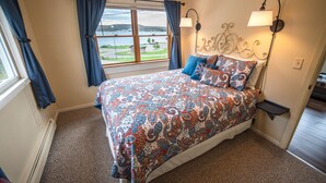 Un dormitorio con una cama grande, vistas a un lago y una mesita de noche con una lámpara.