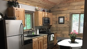 A compact kitchen with wooden cabinets, a refrigerator, a microwave, and a sink. There's a dining table with chairs and a potted plant. -  #1 Fall Creek Cabins 1 mile from Lake Norfork and Mtn. Home Ar. (Mountain Home)