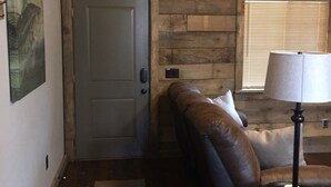 A rustic cabin interior with a wooden wall, a deer head mounted above a door, a couch, a lamp, and a rug. -  #1 Fall Creek Cabins 1 mile from Lake Norfork and Mtn. Home Ar. (Mountain Home)