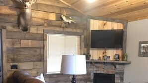 A cozy living room with a stone fireplace, leather armchairs, a lamp, and a mounted deer head on the wall. -  #1 Fall Creek Cabins 1 mile from Lake Norfork and Mtn. Home Ar. (Mountain Home)