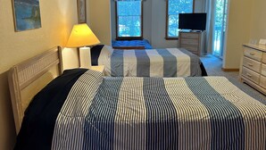 Hotellihuone, jossa on kaksi sänkyä, televisio, lipasto ja ikkuna, jossa on verhot.