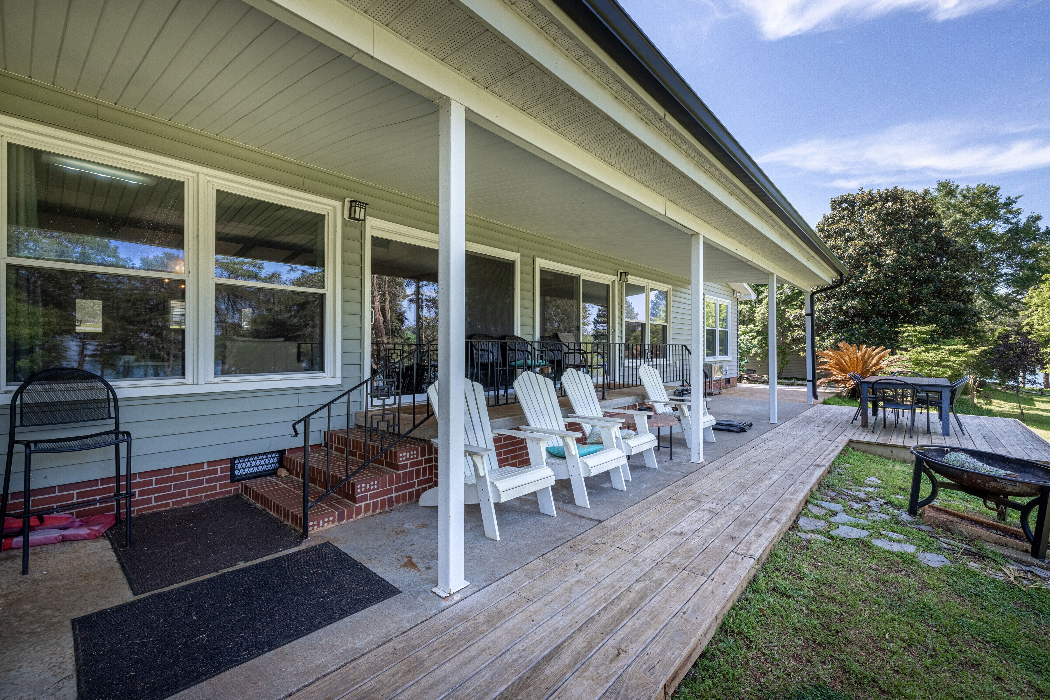 A covered porch with white Adirondack chairs, a table, and a wheelbarrow.