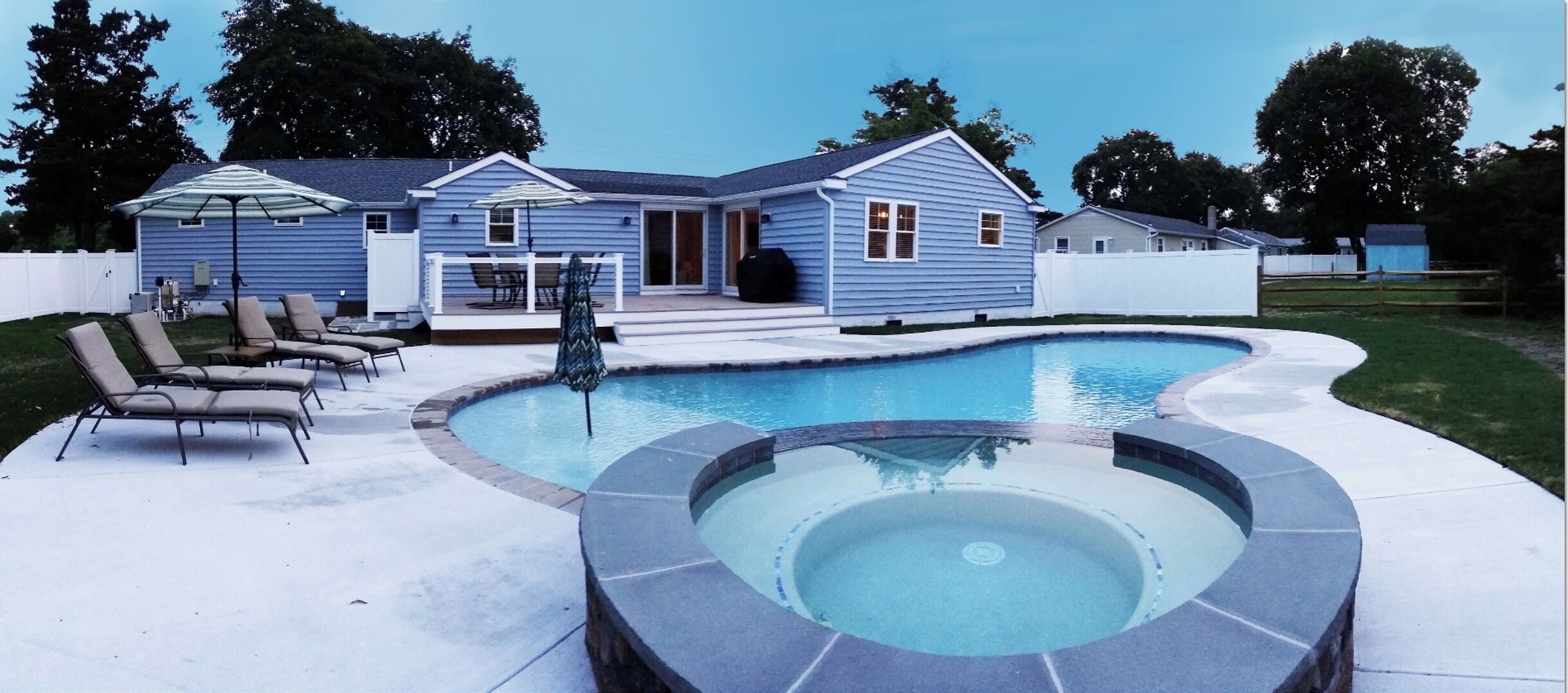 A backyard with a swimming pool, lounge chairs, and a covered patio area.