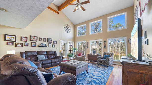 A spacious living room with a large brown leather sofa, a blue patterned rug, and multiple windows offering views of trees. - Hartwell Lake deep water home, family friendly and close to Clemson and UGA (Lavonia)