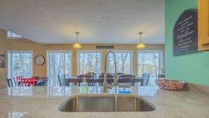 A kitchen with a large island, a sink, and a dining area with chairs and a table. There are windows, a clock, and a sign on the wall. - Hartwell Lake deep water home, family friendly and close to Clemson and UGA (Lavonia)