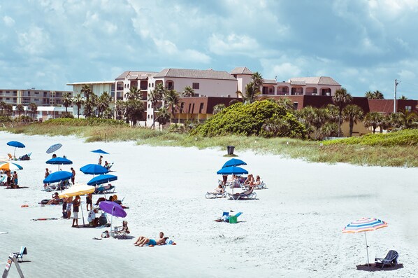 A beach with multiple umbrellas and people relaxing. There are buildings in the background.