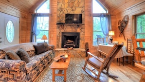 A cozy cabin interior with a stone fireplace, wooden furniture, and large windows. - Beautiful, pet friendly secluded cabin with fire place and hot tub. (Robbinsville)