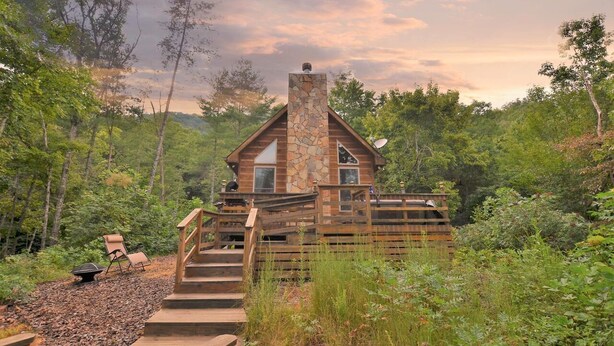 A cabin with a stone chimney, wooden deck, and a view of the surrounding forest. - Beautiful, pet friendly secluded cabin with fire place and hot tub. (Robbinsville)