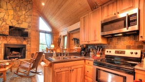 A kitchen with wooden cabinets, a stone wall, a fireplace, and modern appliances. - Beautiful, pet friendly secluded cabin with fire place and hot tub. (Robbinsville)