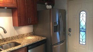 Une cuisine dotée d’un plan de travail en granit, d’un réfrigérateur en acier inoxydable, de meubles en bois et d’une porte blanche agrémentée d’un vitrail décoratif.