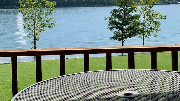 Eine Terrasse mit Metalltisch und -stühlen mit Blick auf einen See, Bäume und eine entfernte Hügelkette.