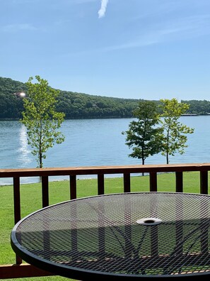 A deck with a metal table and chairs overlooking a lake with trees and a distant hill. - 6 Bedroom Home - Lake Front , Table Rock Lake, Mo. (Shell Knob)