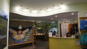 Der Eingang zum Denison Pequotsepos Nature Center mit einer Rezeption, einer großen Eule-Mural und einem Schild, das den Zweck des Zentrums erklärt.