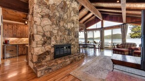 A stone fireplace with a modern design, wooden flooring, and a view of a lake through large windows.