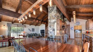 A spacious dining area with a large wooden table and metal chairs, a stone pillar, and a stone fireplace.